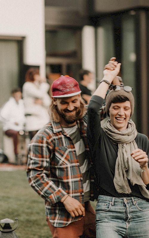 A couple dances happily outside with a band playing in the background. Both are laughing and look relaxed.