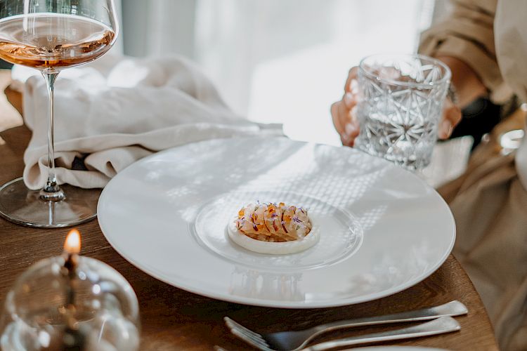 Elegantes Abendessen-Setting mit Gourmet-Vorspeise auf großem weißen Teller, Glas Wein und Wasser.