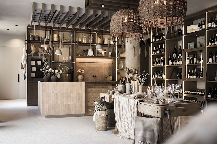 Moderner Weinladen mit hölzernen Regalen, gefüllt mit Flaschen, und rustikalen Dekorationen auf einem Tisch.